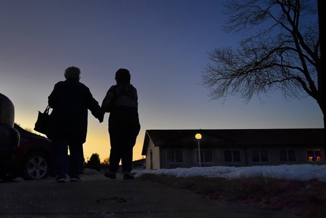 Photo, Elderly adults holding hands leaving nursing home facility 