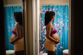 Black pregnant woman stands in bathroom holding stomach