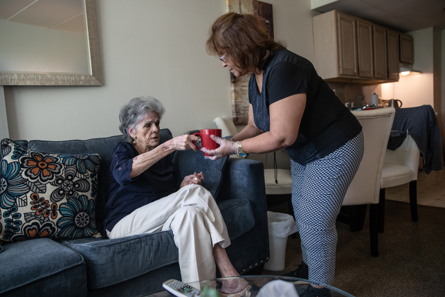 Woman gives cup of tea to elderly woman on couch