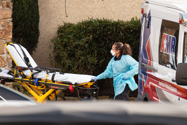 Hospital worker in safety gear loads stretcher out of ambulance