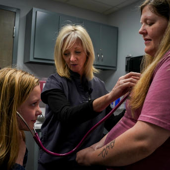 Daughter helps nurse examine pregnant mom in clinic