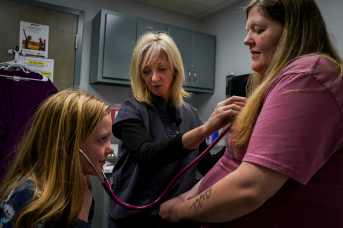 Daughter helps nurse examine pregnant mom in clinic