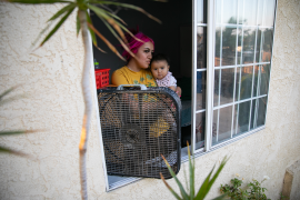 Woman and child stand in front of fan in open window